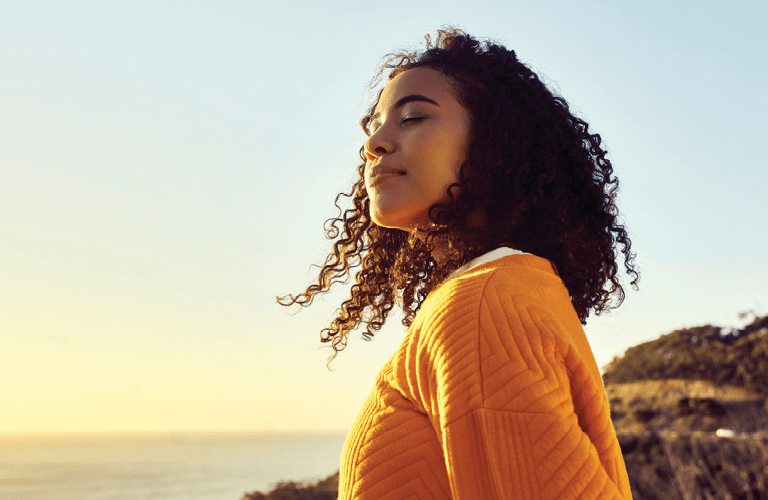 Freedom, relax and happy mindset of a woman from Brazil with sun on her face at a sea. Nature, ocean and beach water sunset with a young person feeling peace, wellness and gratitude from meditation