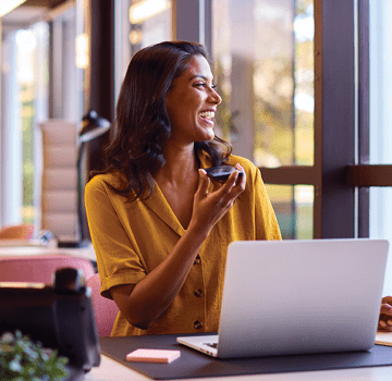 Mature Businesswoman Working On Laptop At Desk In Office Talking Into Mic Of Mobile Phone