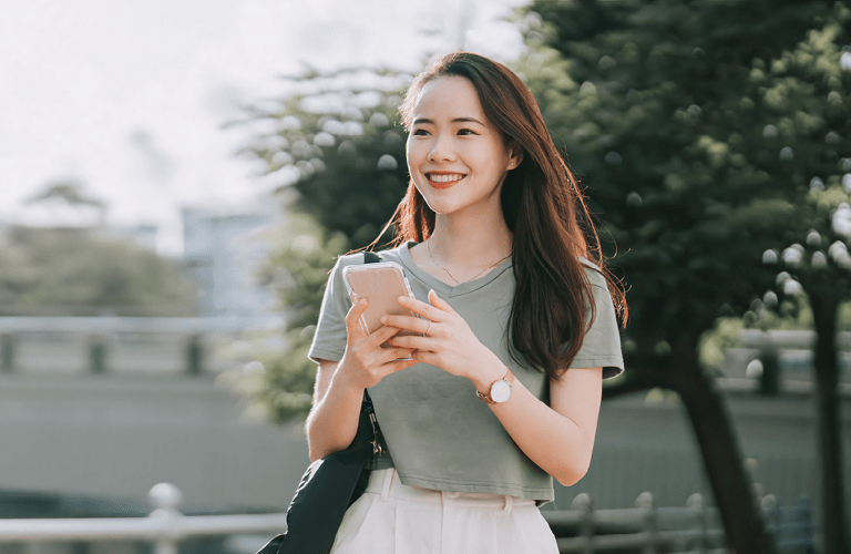 asian Chinese woman walking beside riverbank in the morning with smart phone
