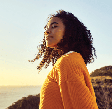Freedom, relax and happy mindset of a woman from Brazil with sun on her face at a sea. Nature, ocean and beach water sunset with a young person feeling peace, wellness and gratitude from meditation