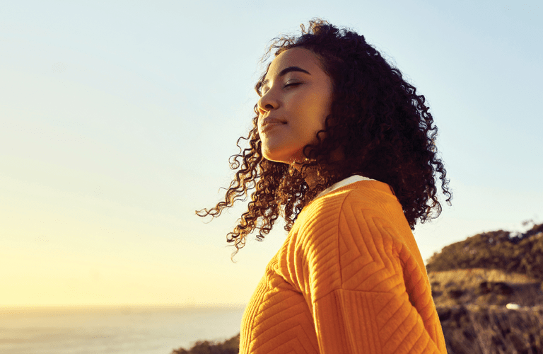 Freedom, relax and happy mindset of a woman from Brazil with sun on her face at a sea. Nature, ocean and beach water sunset with a young person feeling peace, wellness and gratitude from meditation