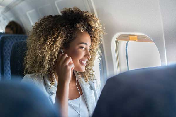Frau im Flugzeug schaut aus dem Fenster und stellt ihren Kopfhörer ein