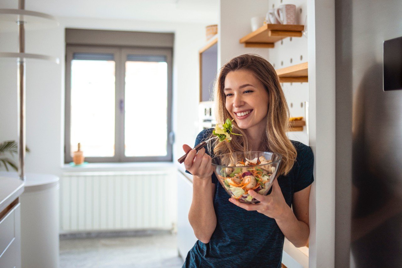 Cheerful woman holding a fresh salad in a home kitchen, promoting healthy eating