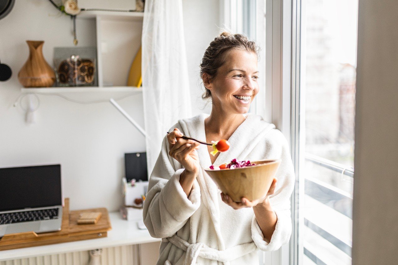 Young woman in a bathrobe enjoying a healthy vegetable salad as part of a nourishing morning routine