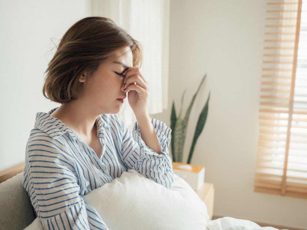 Young Asian woman sitting up in bed looking tired and exhausted in the morning