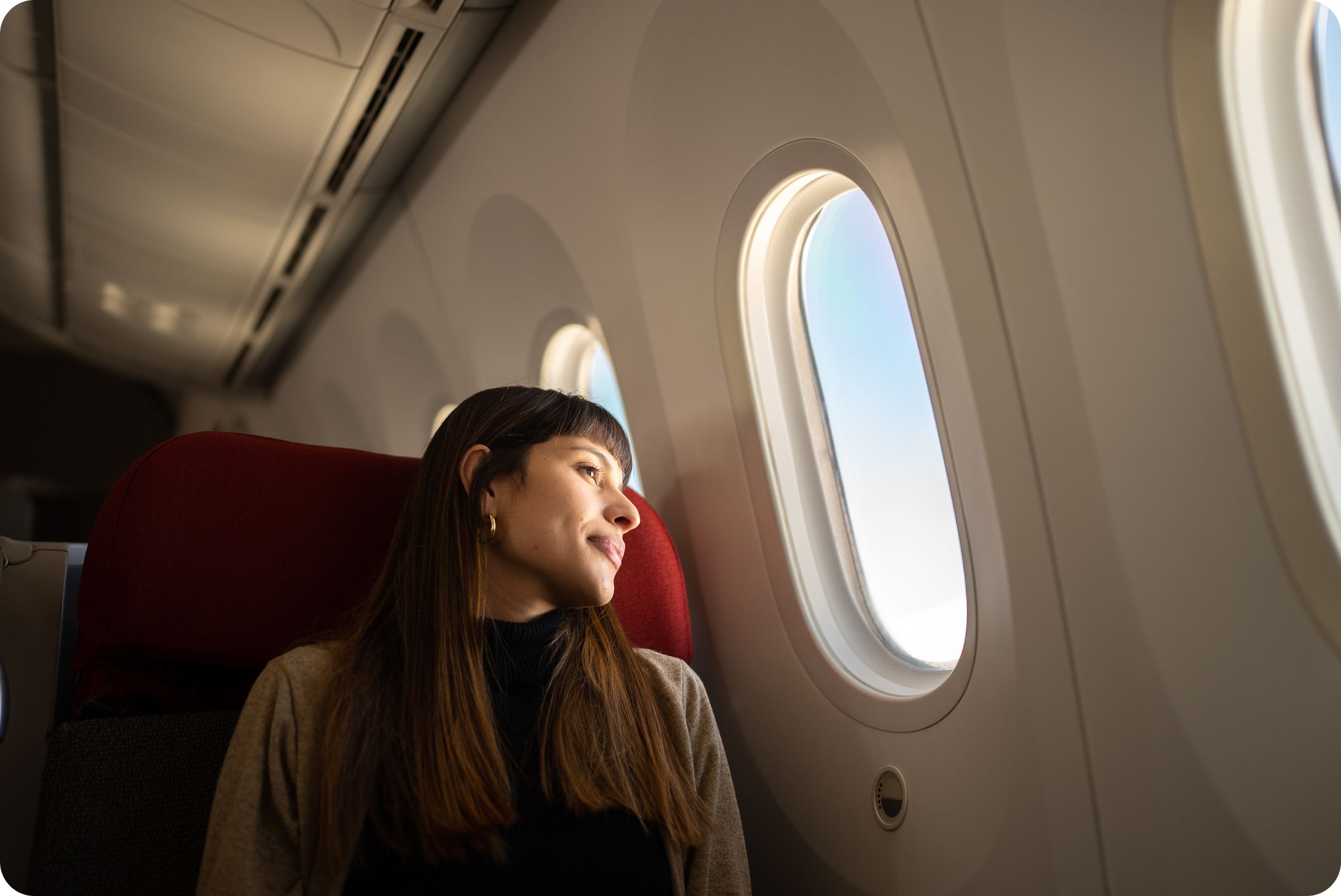 Young woman travelling on a long-haul flight looking out of an airplane window