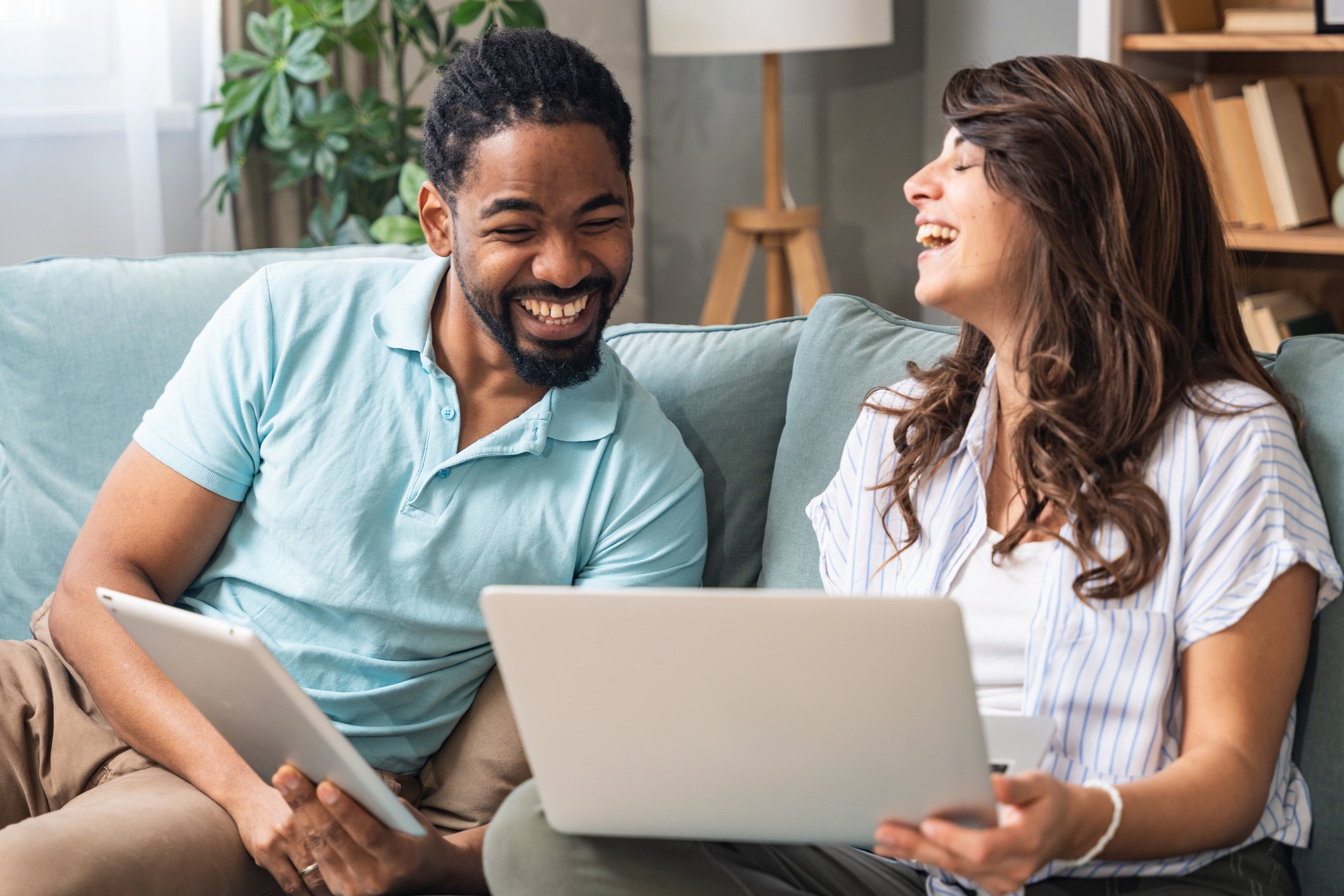 A young woman and man working together on a laptop and tablet, collaborating on a business project in a relaxed and positive home setting.