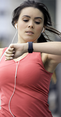 Fit woman jogging outdoors and looking at smartwatch.