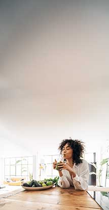 Young African American woman drinking green juice in a loft apartment, highlighting the connection between healthy eating and emotional well-being.