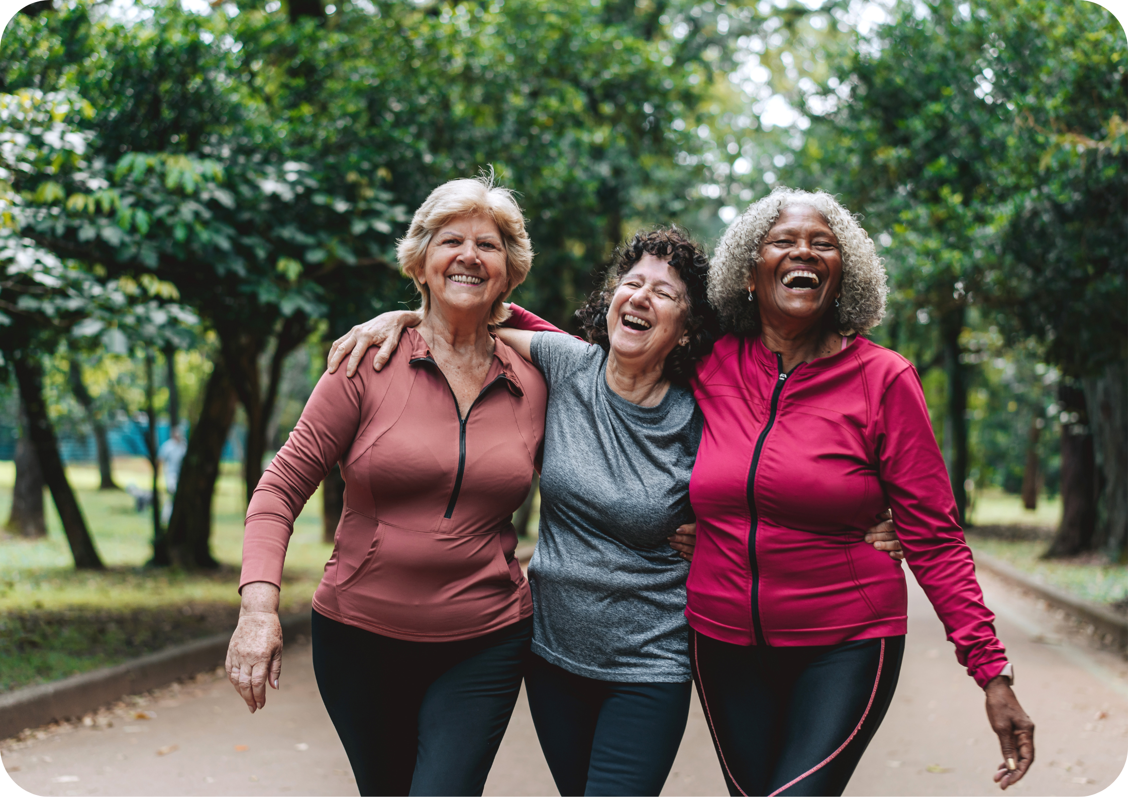 Three women smiling and walking together outdoors in a park