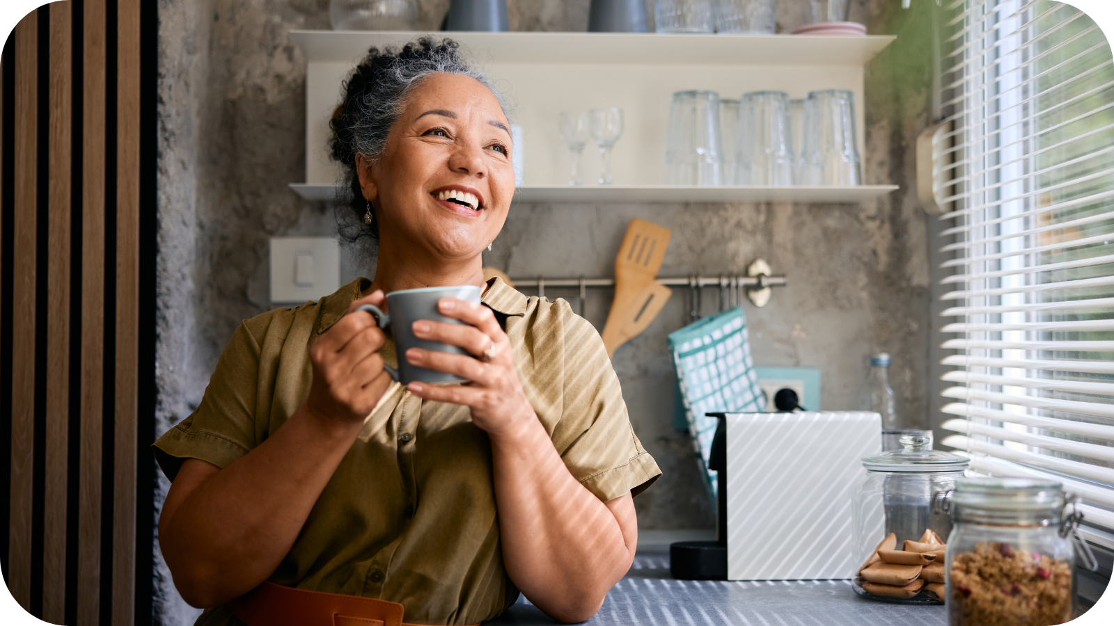 Middle-aged woman smiling and drinking tea by a kitchen window