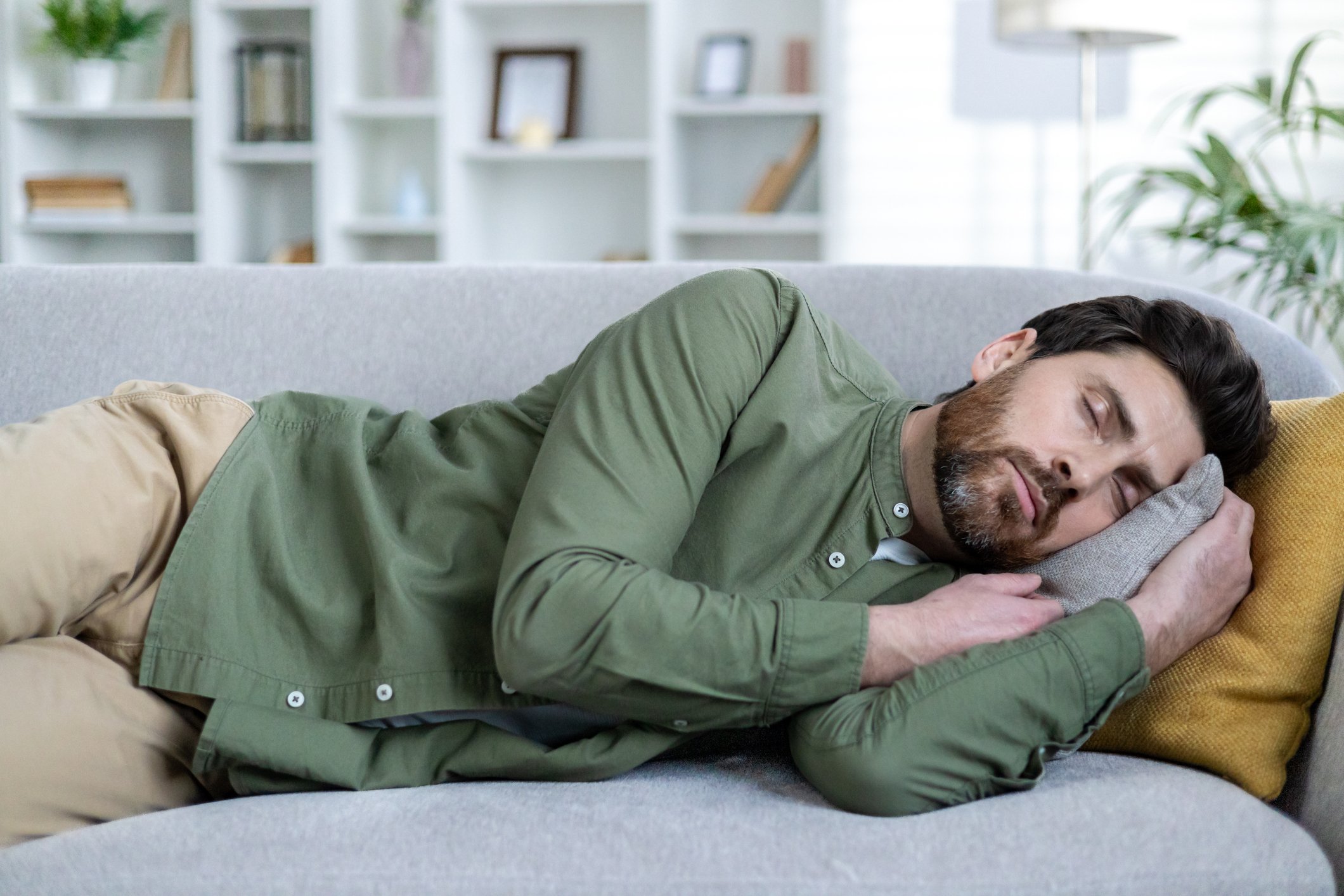 Man napping on a cozy couch in a bright, comfortable living room, reflecting relaxation and rest.