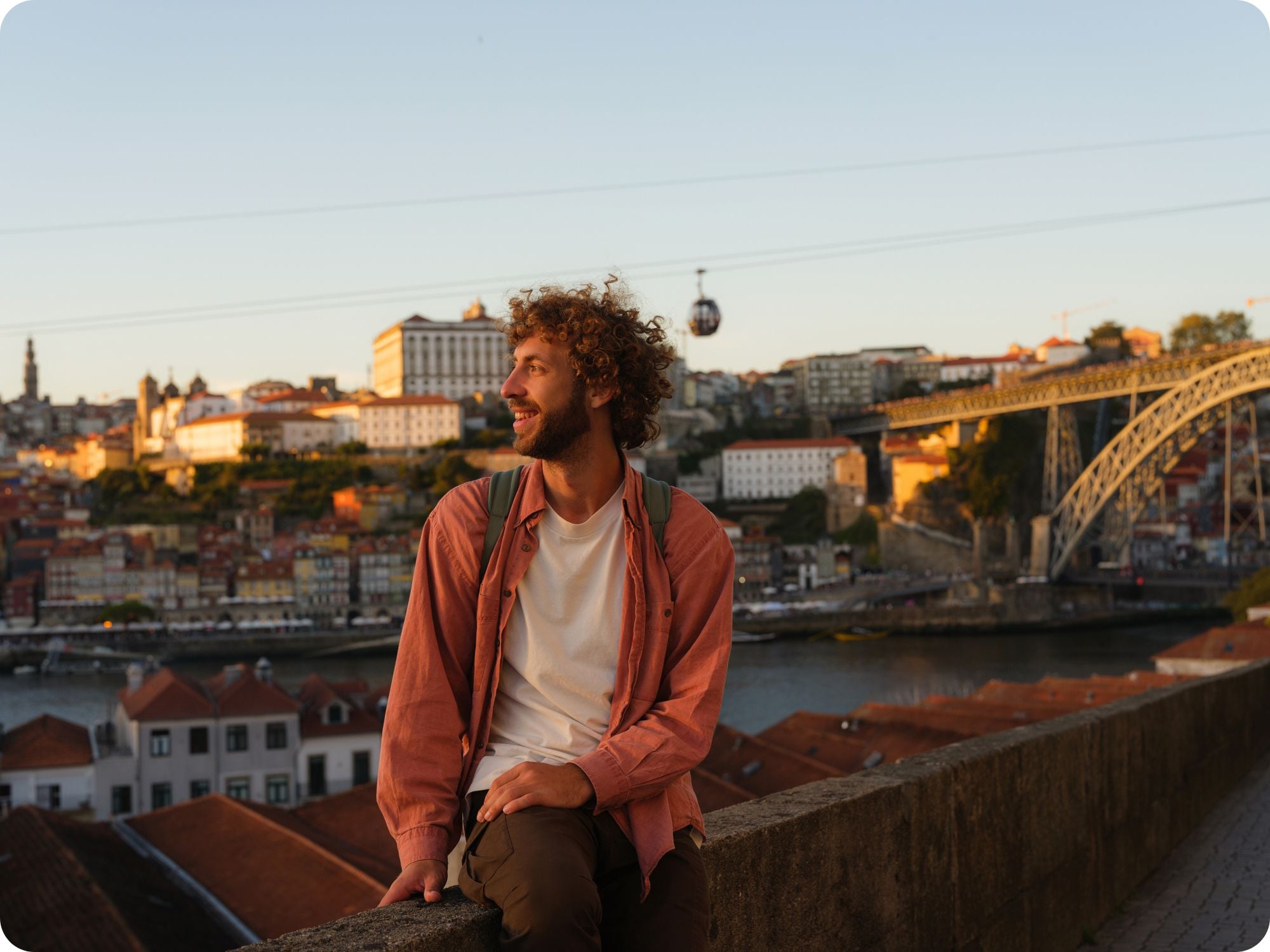 Man with a backpack looking over Porto's cityscape at sunset during a trip to Portugal