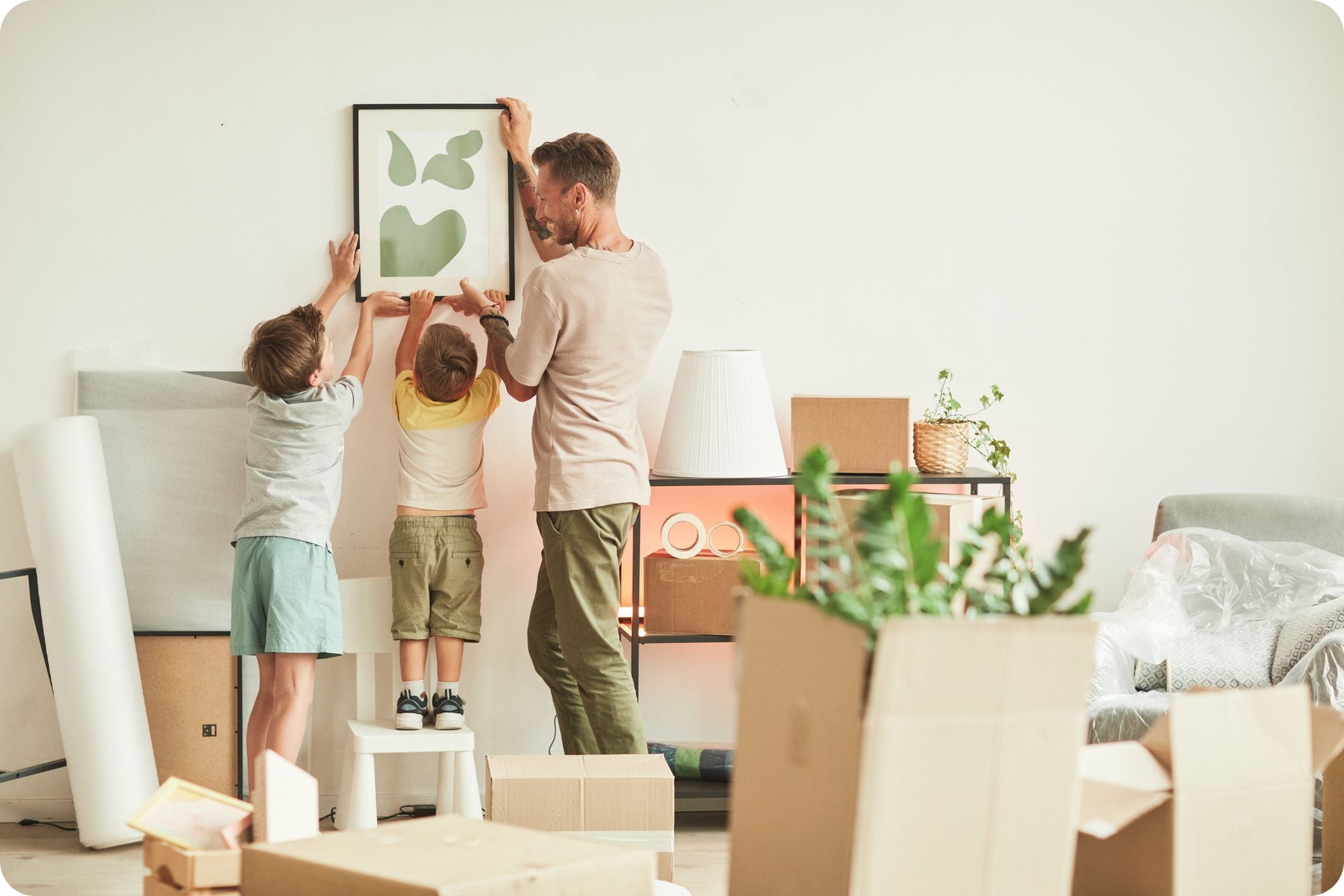 Father and two sons hanging pictures on the wall while moving into their new home