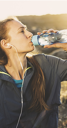 Young woman drinking water after jogging in a sunny scenery. 
