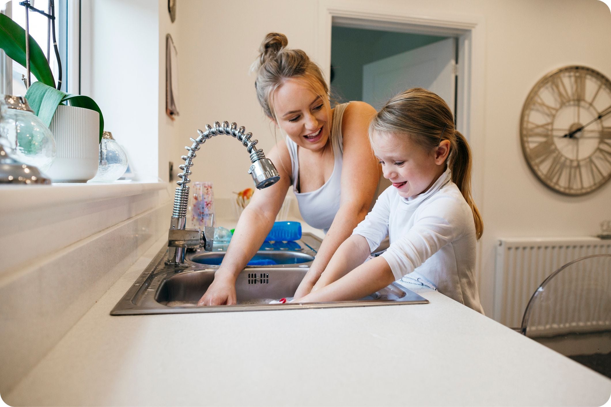 Young girl and her mother washing dishes together at a kitchen sink with the tap turned off