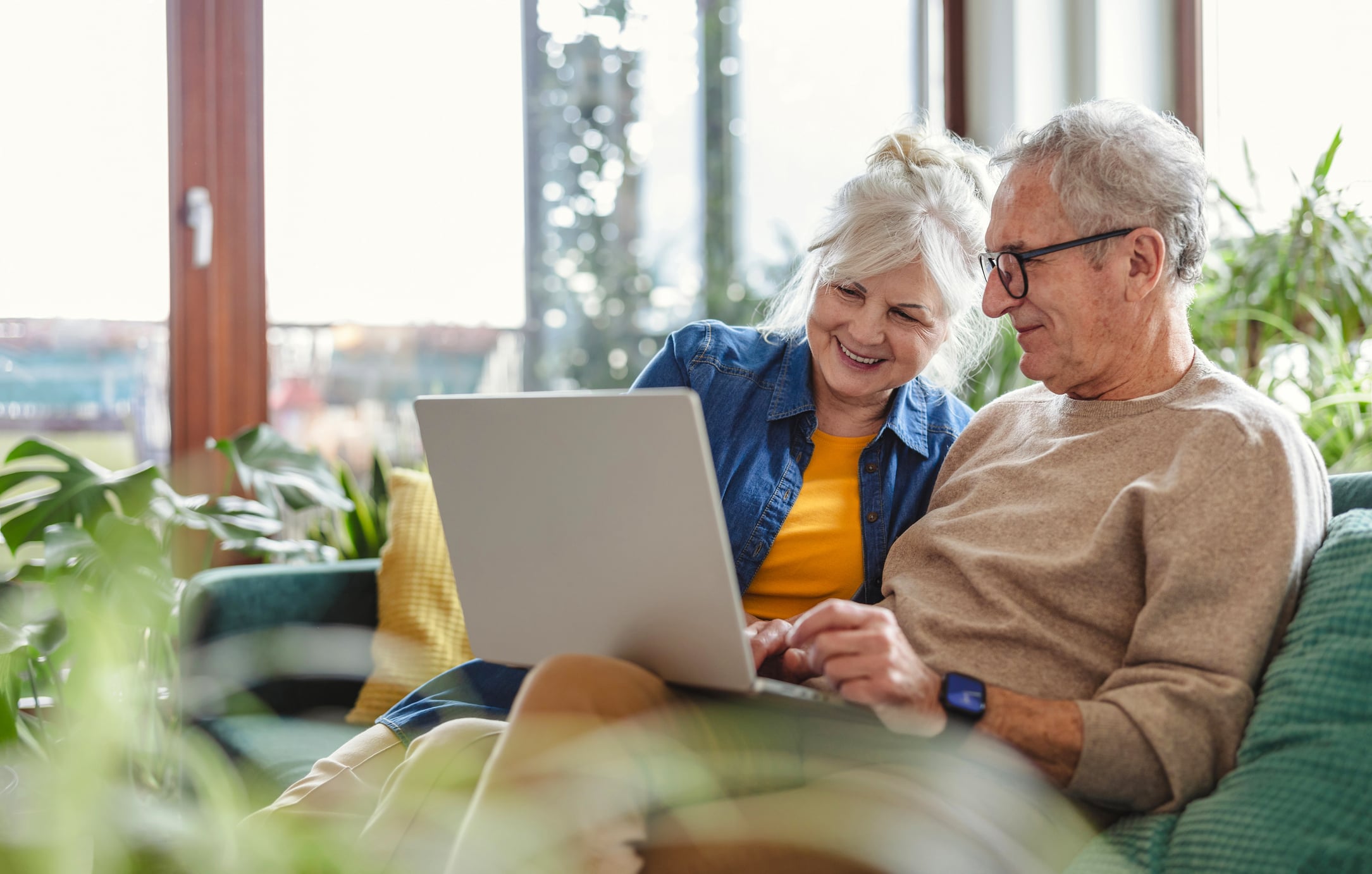 Senior couple sitting on their living room sofa using a laptop