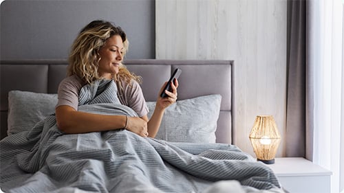 Woman in bed smiling at her phone 