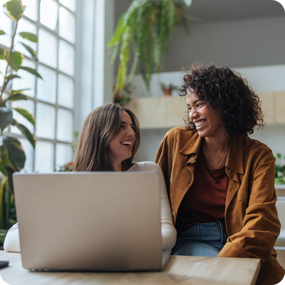 Two young women laughing and working on a laptop at home