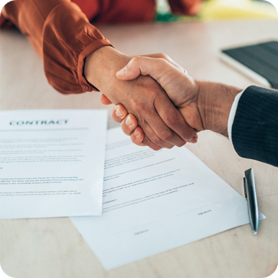 Two professionals shake hands over a signed contract, representing the successful conclusion of a business deal.
