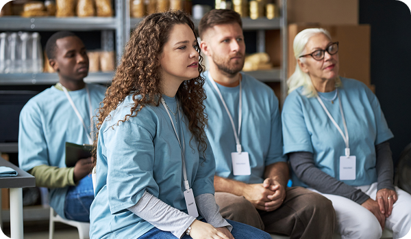 Diverse group of volunteers sitting together, wearing matching blue shirts and name tags, attentively listening during meeting