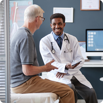 Smiling Black Doctor Holding Tablet Talking to Senior Patient in Consultation
