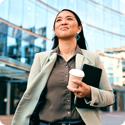 Confident Businesswoman Walking with Coffee Outside Modern Office Building