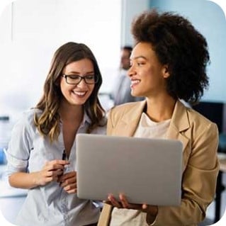 Two happy and smiling businesswomen collaborating online, working together on a laptop in a modern office setting