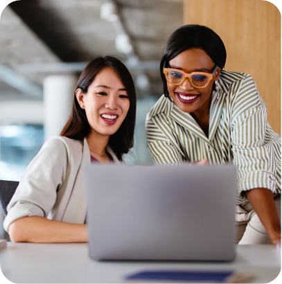 Two professional women discussing work on a laptop, demonstrating teamwork and collaboration in a modern office setting.