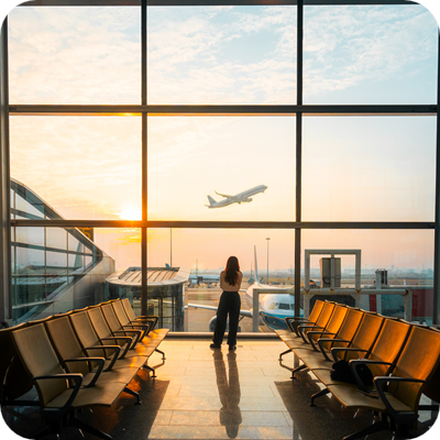 A young women is looking out of a large window at the airport