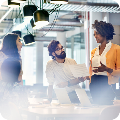 Business people looking at female colleague explaining documents while standing at conference table.