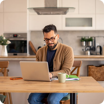 Mid-Aged Professional In Cardigan Working On Laptop In Contemporary White Kitchen 