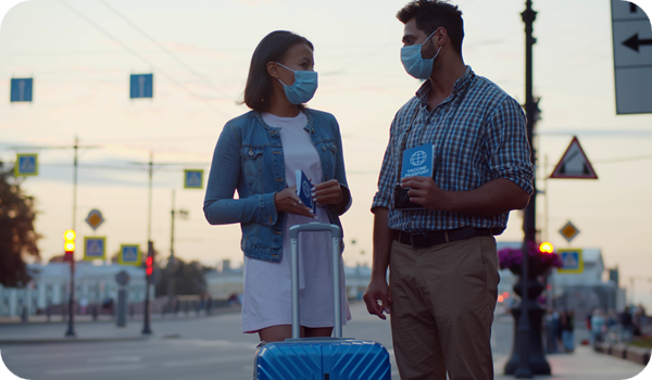 Multiethnic couple in safety mask standing outdoors with luggage and vaccine certificate 
