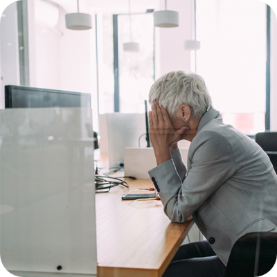 Frustrated woman with head in hands sitting on desk in the office.