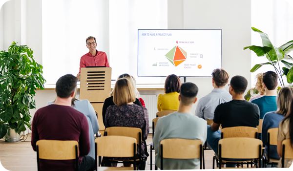 A seminar host standing behind a podium and giving a presentation to a small audience.