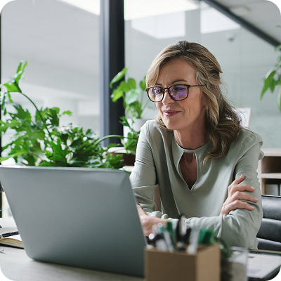 Laptop, arms crossed and mature business woman at desk in glass office.