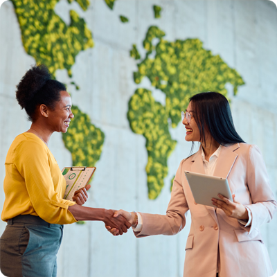 Two smiling businesswomen shaking hands in modern office with moss wall map 