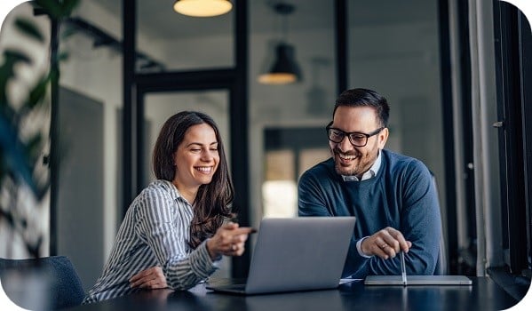 A businessman and a businesswoman smiling in a meeting room, using a laptop