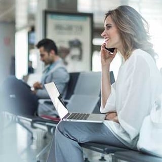 Young woman working on a laptop and using a phone while sitting at an airport departure gate
