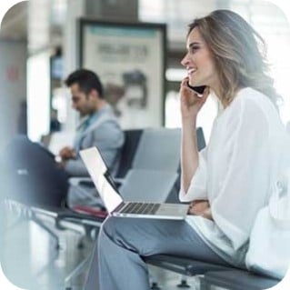 Young woman working on a laptop and using a phone while sitting at an airport departure gate