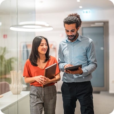 Two diverse colleagues in smart casual attire discussing a digital tablet in a modern office, representing teamwork and productivity.