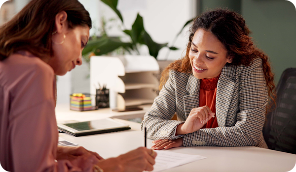 Human resource manager sits in an office with a female business woman, signing paperwork