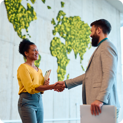 Businesspeople shaking hands in front of a world map made of plants