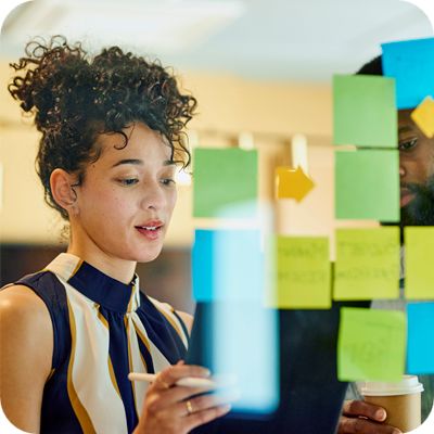 A man and a woman are standing in front of a glass wall writing on sticky notes.