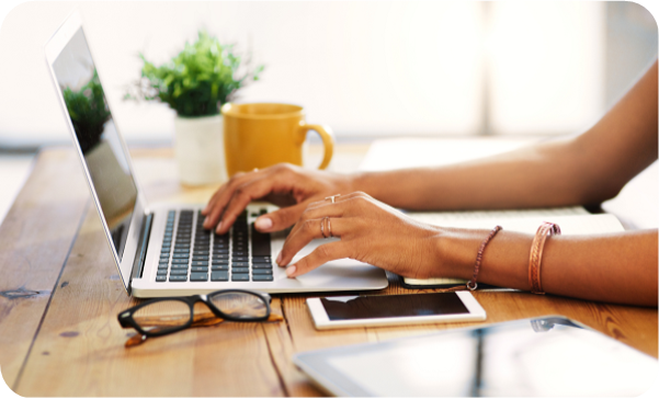 Woman typing on laptop, her glasses and phone laying next to her. 