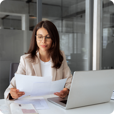 Concentrated latin business woman saleswoman working on laptop computer reading financial bank tax document in office workplace.
