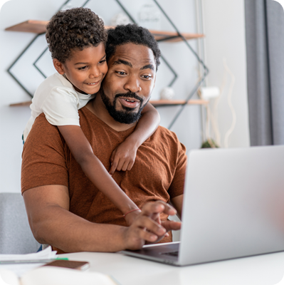 African American father using laptop and working at home while being distracted by his son.