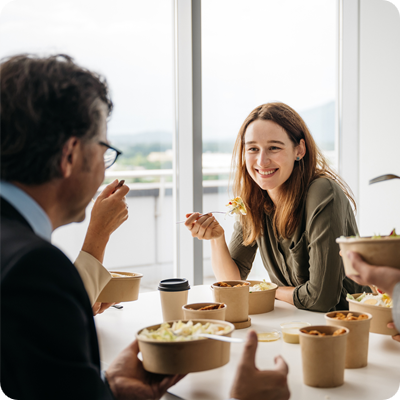 A smiling woman is enjoying a healthy takeaway lunch with her colleagues in a bright modern office. 