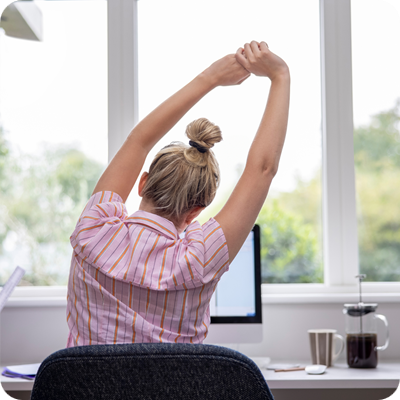 Rear View Of Woman Working From Home On Computer In Home Office Stretching At Desk
