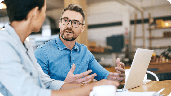 Two professionals having a discussion at a table with a laptop